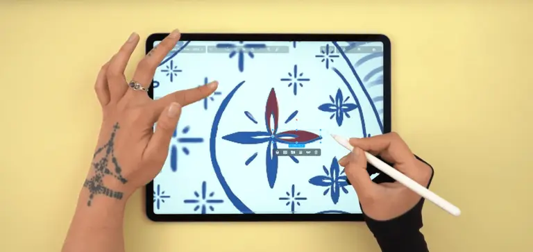 Hands using a stylus on a tablet to create a blue floral design