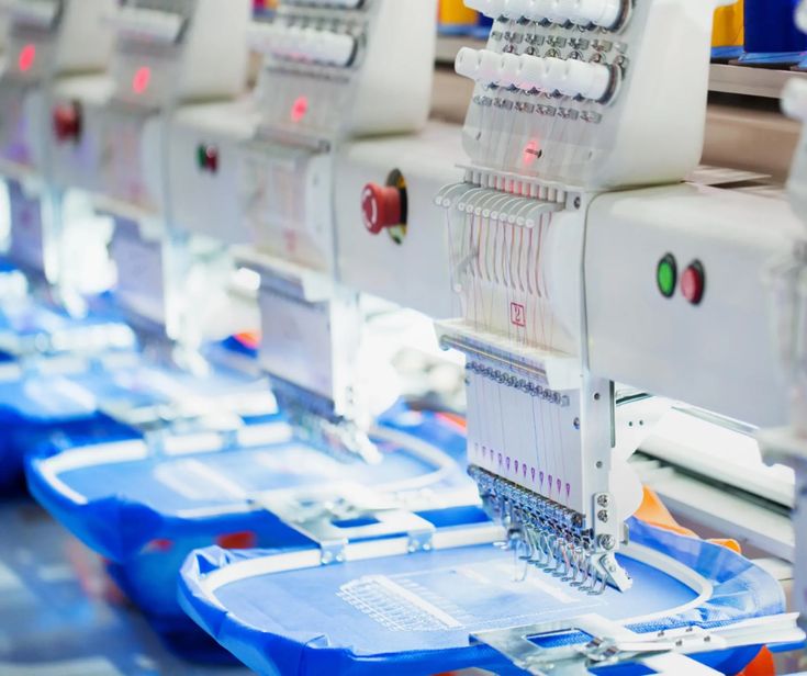 Close-up of multiple computerized embroidery machines stitching designs onto blue fabric in a production line.